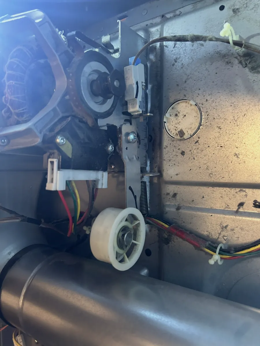 Inside a clothes dryer showing the motor, idler pulley and belt path